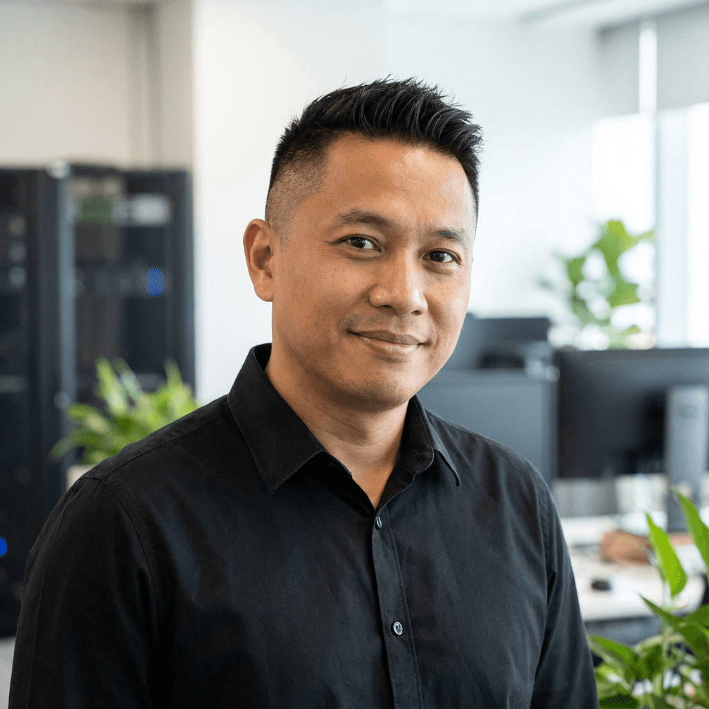 Smiling man with short dark hair wearing a black shirt in a modern office environment.